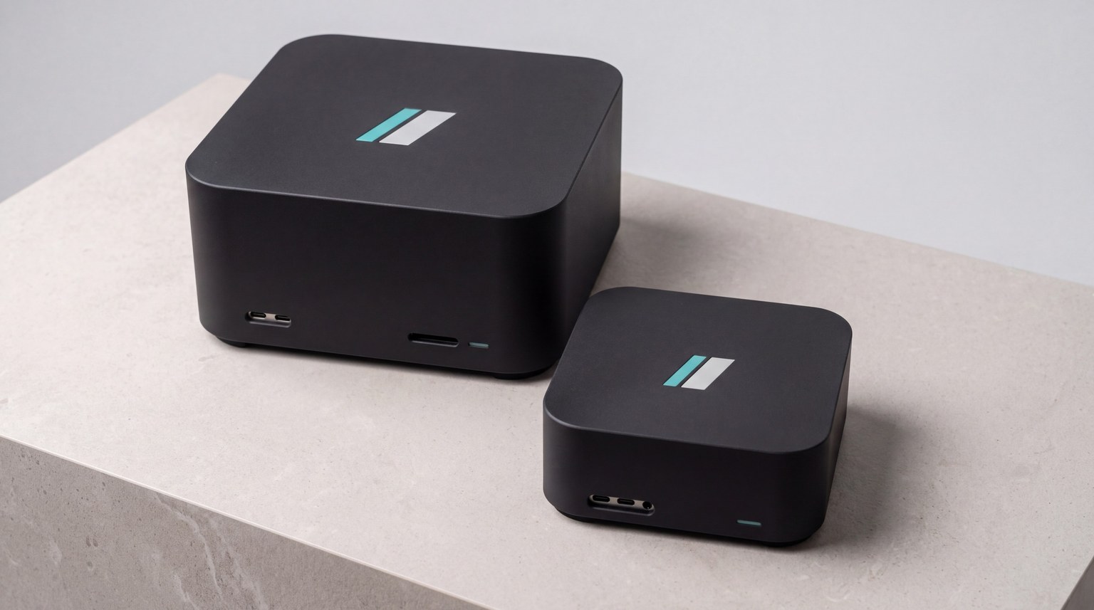 Two satin-black razorBridge appliances on a stone plinth: the larger Outpost Blade and the compact Outpost. Each carries the razorBridge mark inlaid in its lid and a thin teal status light.